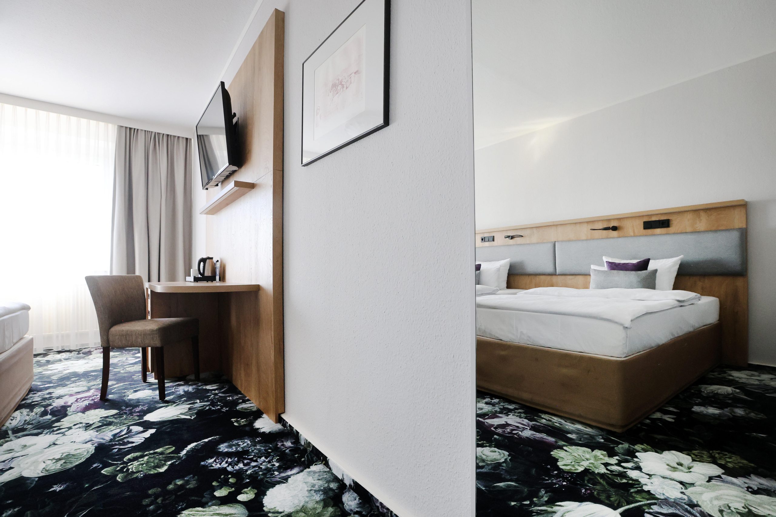 Best Western Hotel Windorf Plüss Raumgestaltung Modernes Hotelzimmer mit floralem Teppich, Holzdetails und funktionaler Raumaufteilung – Maßgeschneiderte Lösungen für jedes Raumkonzept von Raumgestaltung René Plüss aus Leipzig