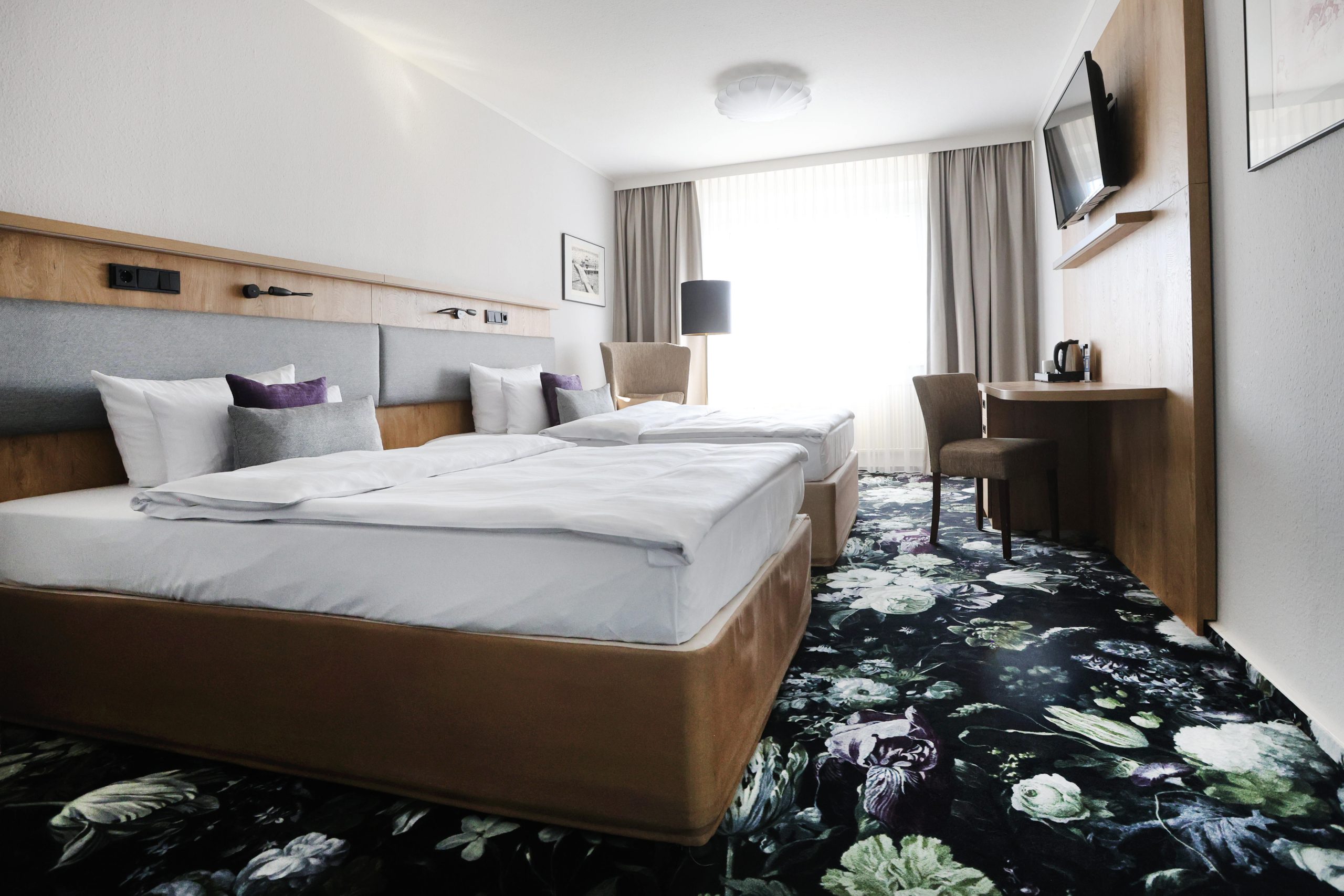 Best Western Hotel Windorf Plüss Raumgestaltung Modernes Hotelzimmer mit floralem Teppich, Holzdetails und funktionaler Raumaufteilung – Maßgeschneiderte Lösungen für jedes Raumkonzept von Raumgestaltung René Plüss aus Leipzig