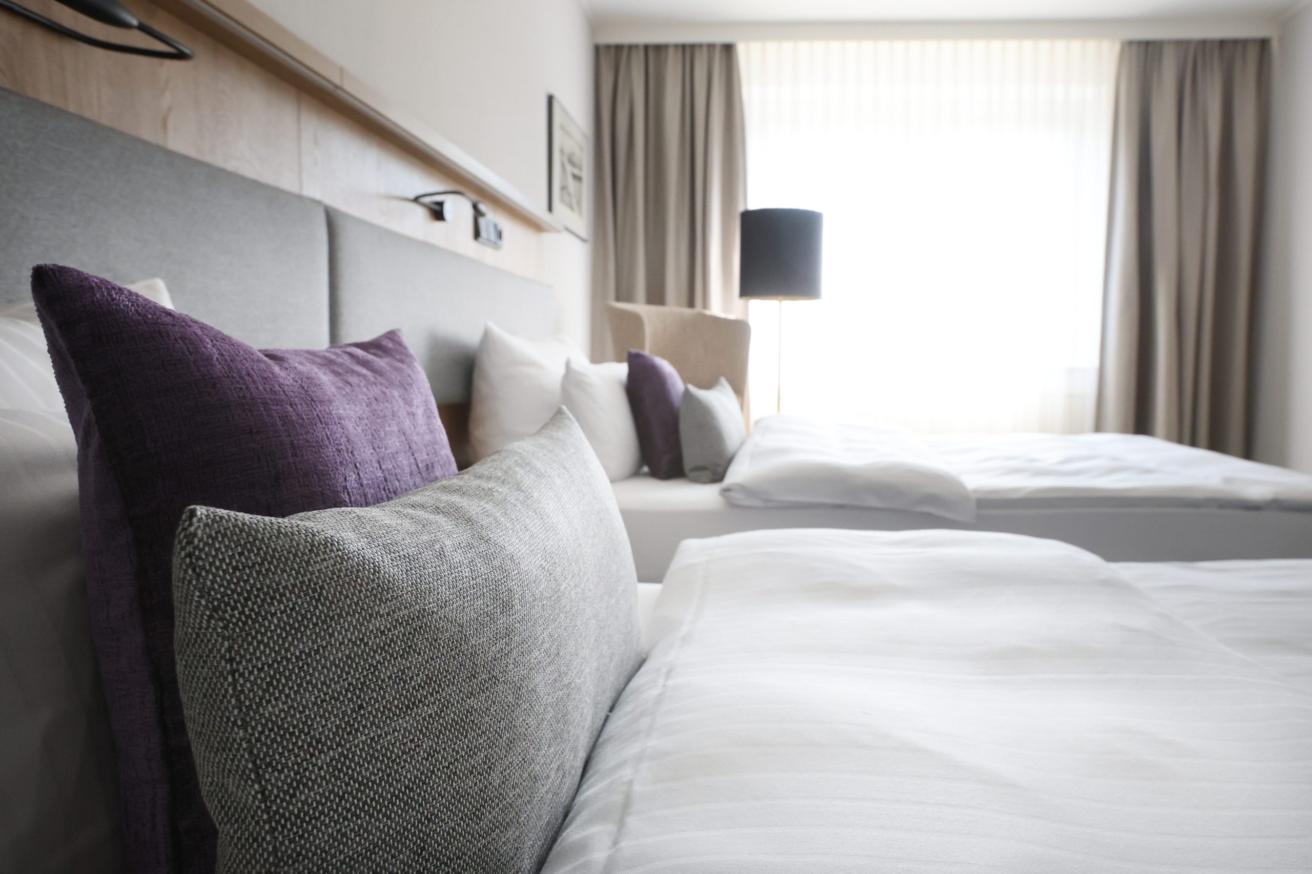 Best Western Hotel Windorf Raumgestaltung René Plüss Leipzig Hochwertige Kissen in Lila und Grau auf einem Hotelbett vor einem lichtdurchfluteten Fenster – Maßgeschneiderte Lösungen für jedes Raumkonzept von Raumgestaltung René Plüss aus Leipzig
