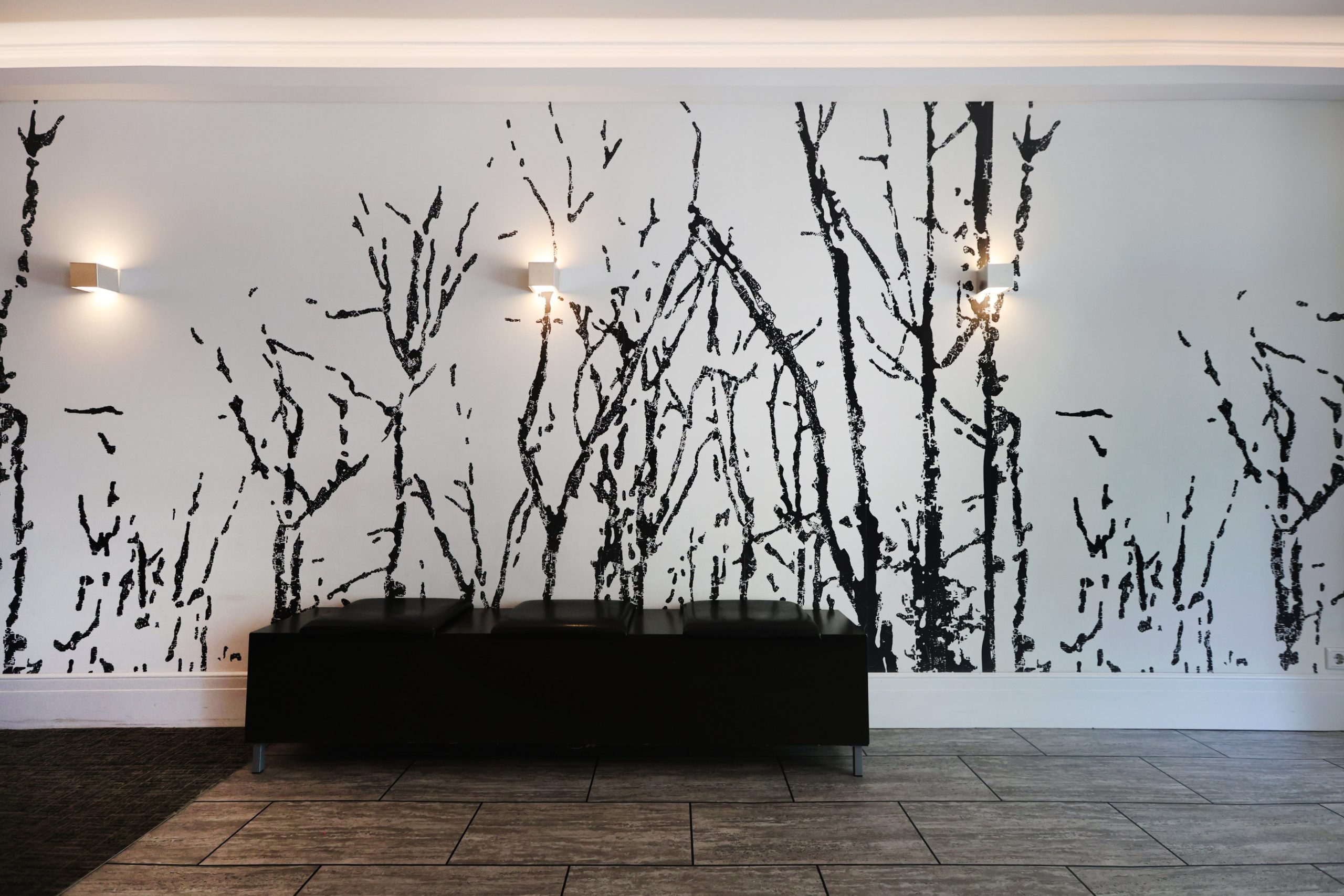 Wandgestaltung mit grafischem Baum-Motiv Raumgestaltung René Plüss Leipzig Moderne Wandgestaltung mit schwarz-weißer Baumgrafik und minimalistischer Bank – Maßgeschneiderte Lösungen für jedes Raumkonzept von Raumgestaltung René Plüss aus Leipzig